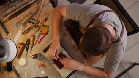 worker taps tool with hammer to make holes in leather