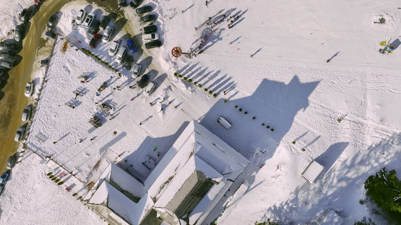 Aerial View of a Snowy Ski Resort with People, Buildings, and Parked Cars