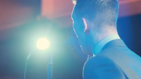 man singing song in microphone during performance on stage on rock concert. close up man rock star singer on music concert on colorful light background