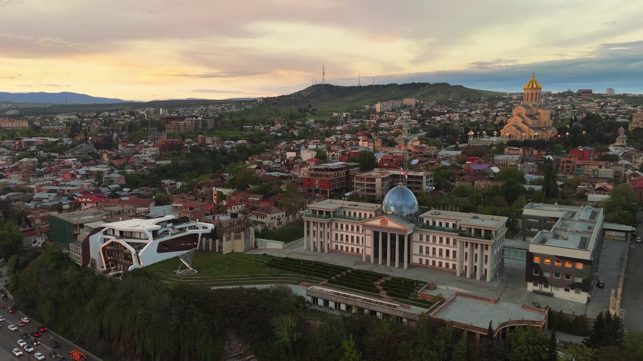 Letecký pohled na Prezidentský palác Gruzie a katedrálu Nejsvětější Trojice v Tbilisi (Sameba) za soumraku, ukazující směs klasické a moderní architektury v hlavním městě