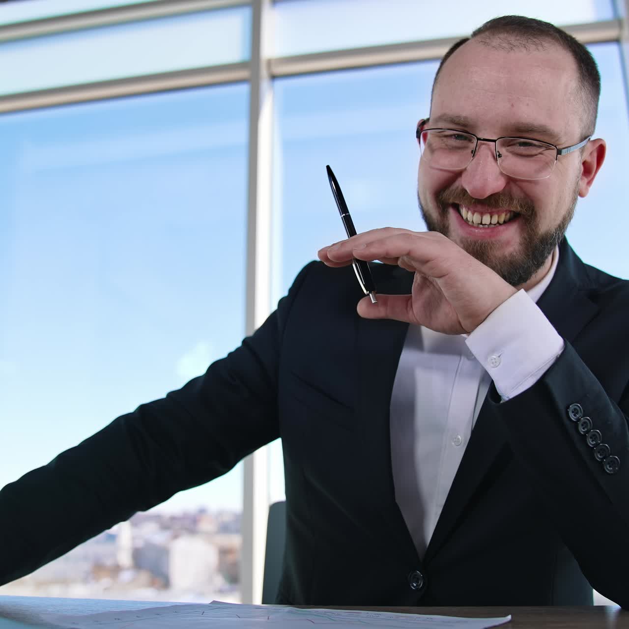 Retrato de empresário positivo. Empreendedor de sucesso sentado à mesa e olhando para a câmera. Chefe barbudo de óculos e terno elegante no escritório