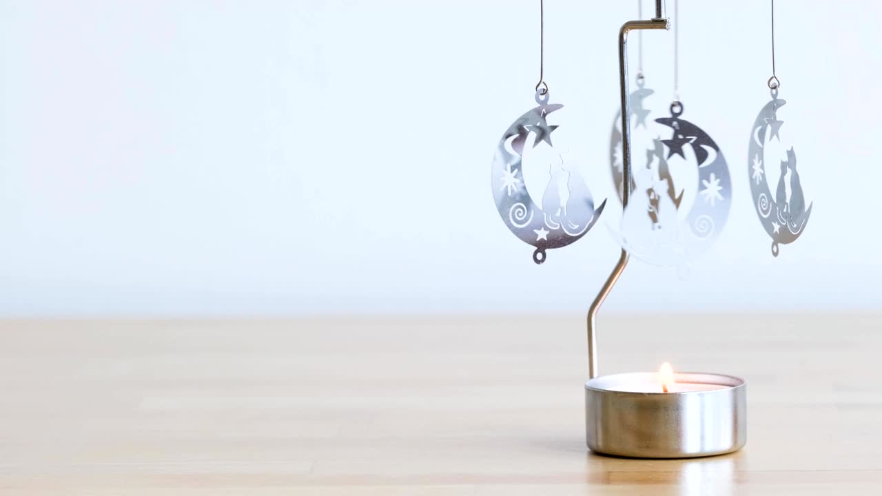carrusel giratorio de metal con vela ardiente y motivo de gatos y lunas en mesa de madera