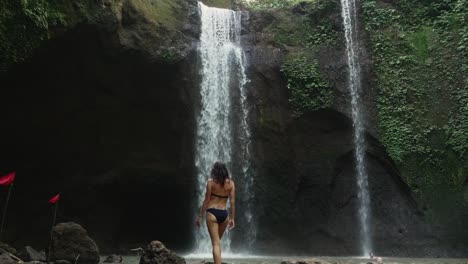 una niña caminando lentamente hacia la cascada y mirándola