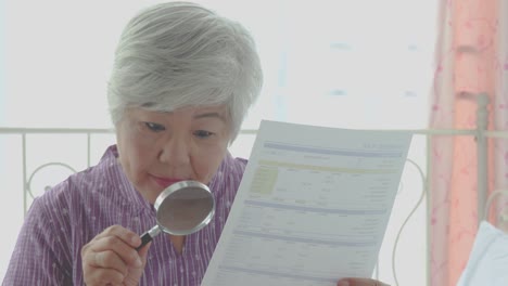 elderly woman using a magnifying glass to reading through the lens to handheld document as her eyesight deteriorates with age