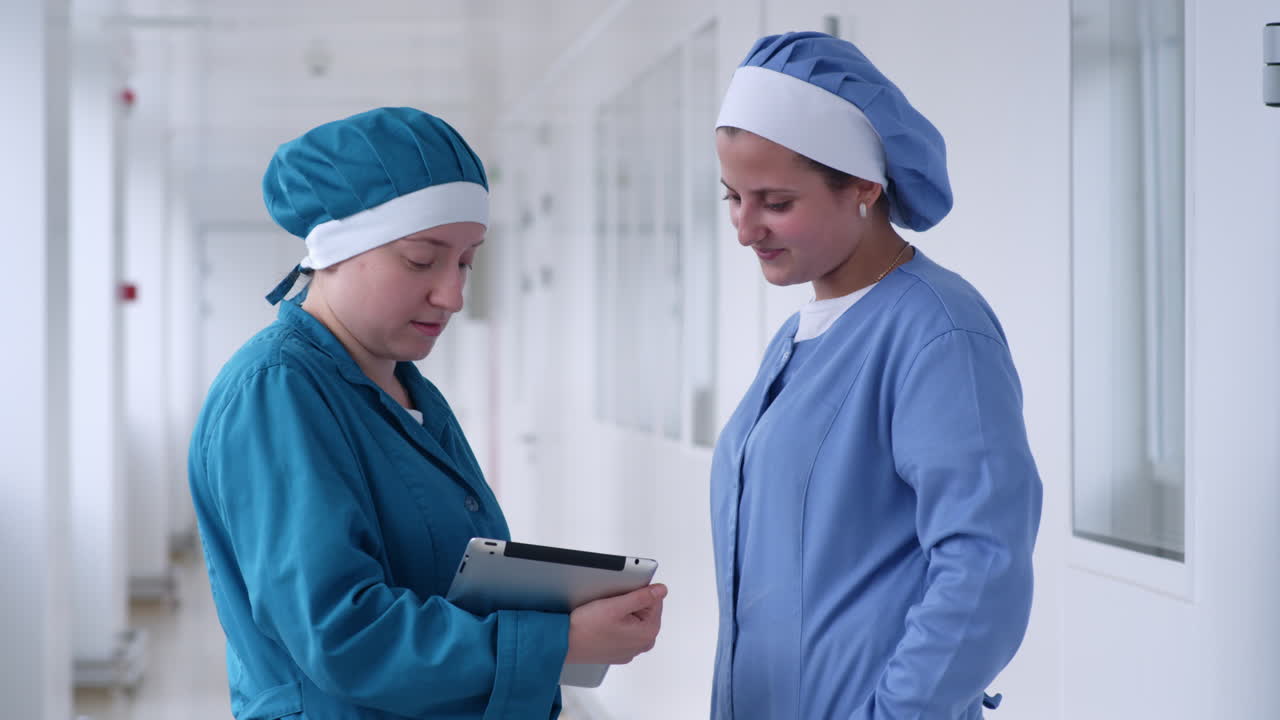 dos mujeres usando la tableta en el pasillo blanco. mujeres de laboratorio buscando la tableta y sonriendo