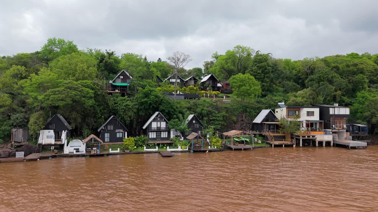 Drone view of modern riverside glamping houses surrounded by lush forest on Parana River, eco-tourism, Puerto Lagier, Misiones, Argentina