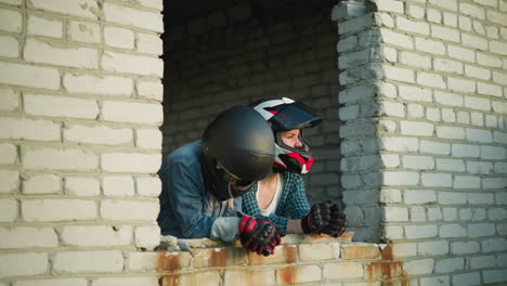 two women in helmets leaning on the ledge of an old building window, one woman looks into the distance while the other is lifting her head after gazing downward