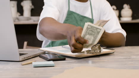 male small business owner counting money and writing on clipboard in the pottery shop 1