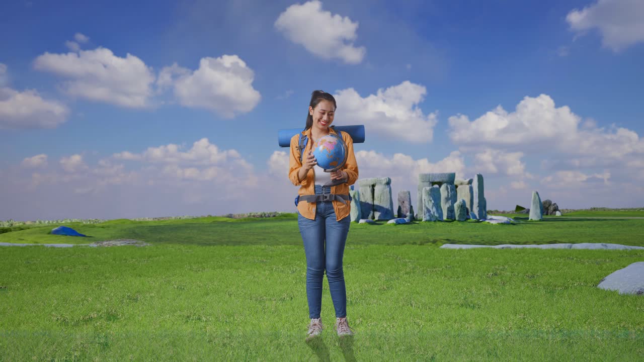 Full Body Of Asian Female Hiker With Mountaineering Backpack Holding World Globe In Her Hands And Smiling While Traveling In Stonehenge