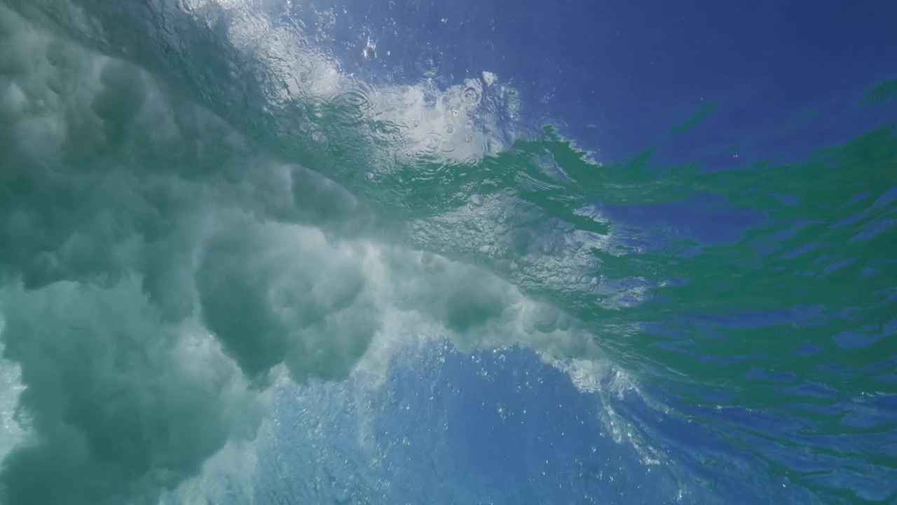 Ocean wave passes overhead through clear turquoise water with a softly illuminated surface below