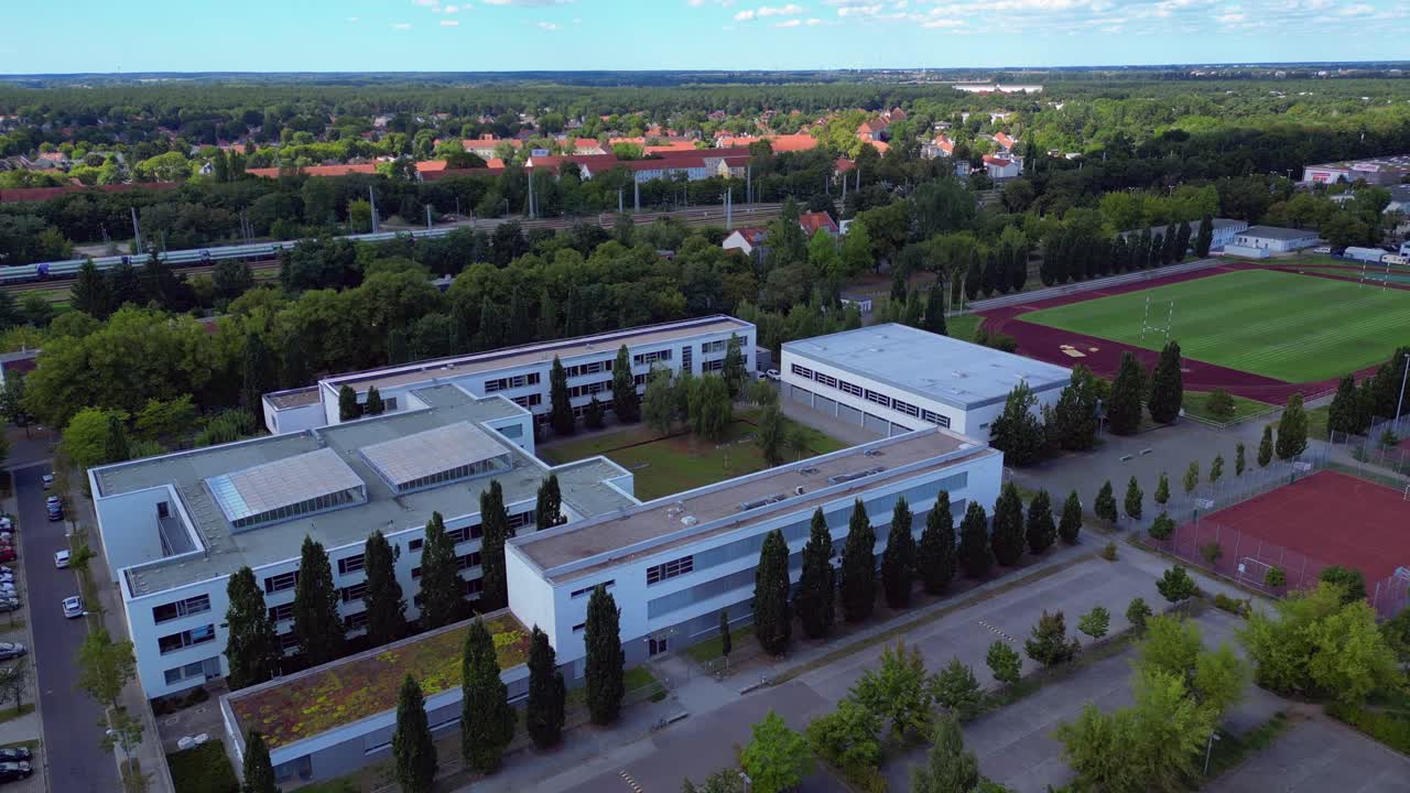 Hennigsdorf High School showcasing its modern architecture, sports facilities, parking area, surrounding urban landscape. Spectacular aerial view flight static tripod hovering drone