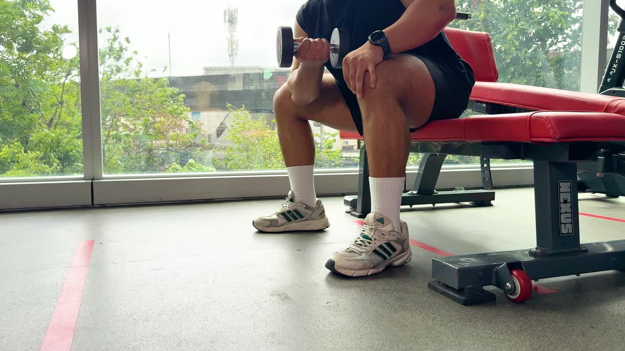 Athletic man lifts dumbbell on bench in bright gym, natural daylight, steady camera, focused mood