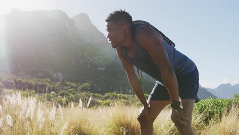 hombre afroamericano haciendo ejercicio al aire libre apoyado en sus rodillas en el campo en una montaña