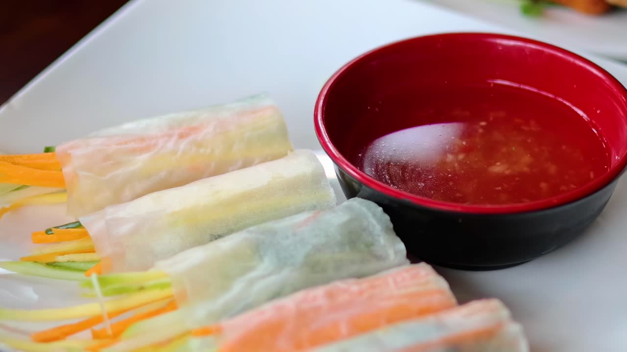 Close-up of vibrant spring rolls and red dipping sauce on a white plate.