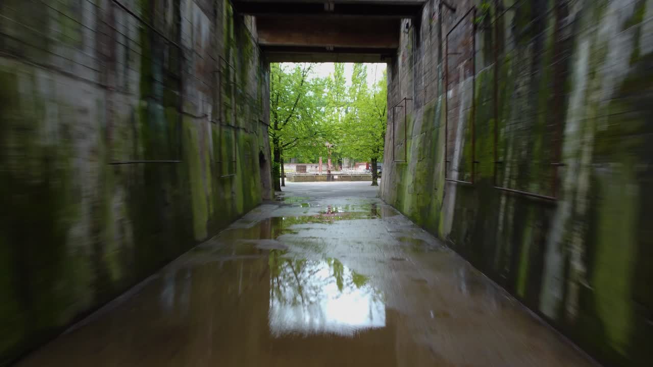 estrecho callejón con un túnel de piedra las paredes del túnel están hechas de hormigón y tienen varias ventanas a lo largo de ellos hay una pasarela que atraviesa el centro del túnel árboles en el otro lado