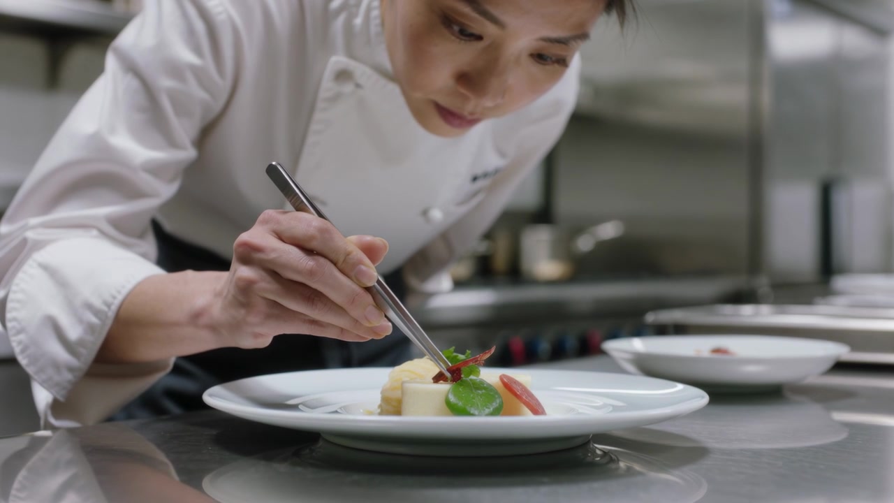 Orders arriving, Asian chef in chef coat placing microgreen with tweezers at restaurant for service