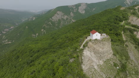 high angle aerial shot of a small building surrounded with forested hills