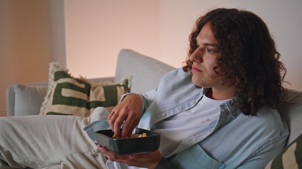 Resting man enjoying movie on television lying home couch with snacks closeup