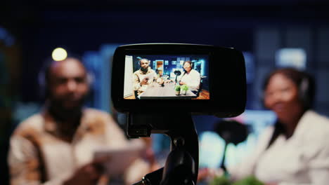 focus on vlogging camera used by cohosts in blurry background streaming podcast during live debate