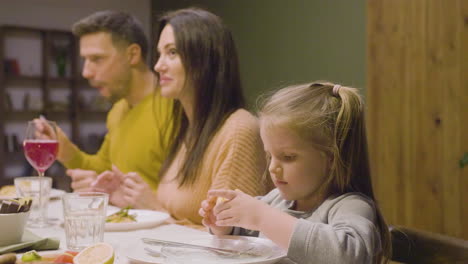 little blonde girl sitting near her parents at a family dinner