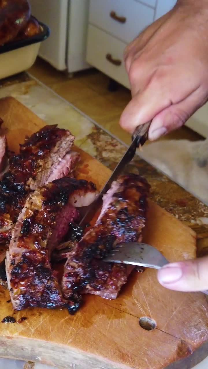 Vertical close up hands cutting asado red meat with knife, traditional argentine and south american barbecue