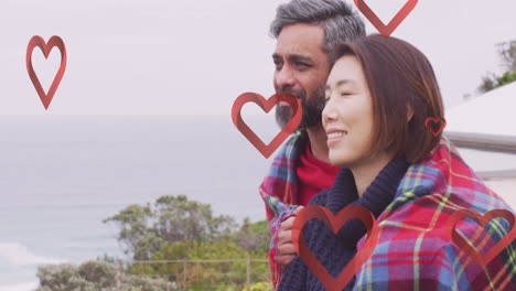 Animation-of-hearts-over-diverse-couple-embracing-on-balcony