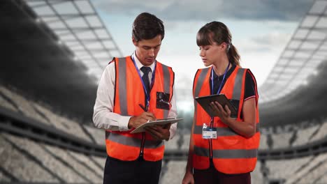 animation of stadium over caucasian male and female workers talking and using tablet