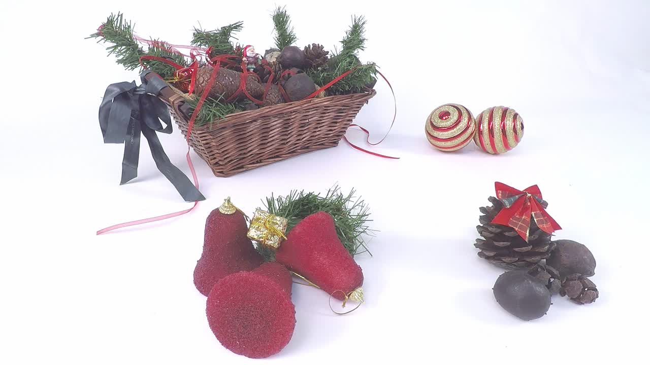 artículos decorativos de navidad sobre fondo blanco con cesta de madera, hojas de pino, conos de pino, campanas rojas, bolas de navidad, honda de madera y cláusulas de papá noel