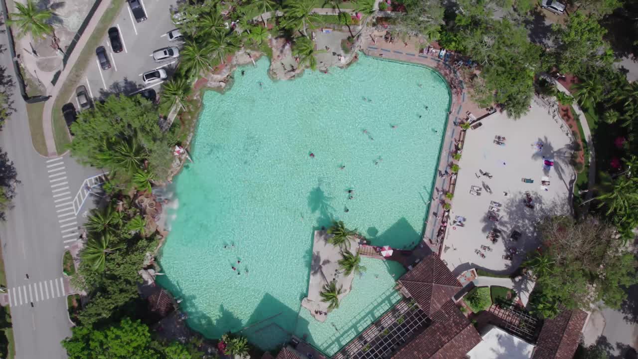 Voo panorâmico de drone circulando a Piscina Veneziana, destacando o contraste entre a lagoa turquesa e as exuberantes figueiras-de-bengala de Coral Gables.