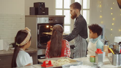 Niños-Y-Chef-Poniendo-Una-Bandeja-Para-Hornear-En-El-Horno-Durante-La-Clase-De-Cocina