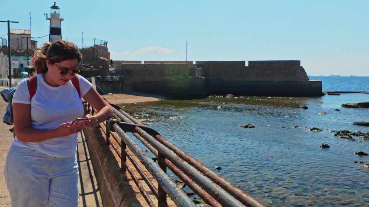 Young female tourist checking smartphone near the ancient lighthouse in Acre