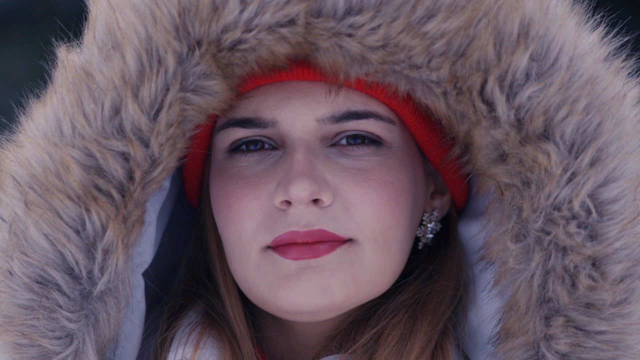 Tight portrait of a woman looking at camera wearing a large fur hood in snowy forest.