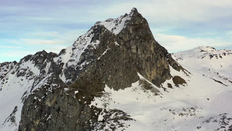 Disparo-De-Drones-Volando-Hacia-El-Pico-De-Una-Montaña-Rocosa-Con-Campos-De-Nieve-A-Ambos-Lados,-En-La-Plagne,-Francia