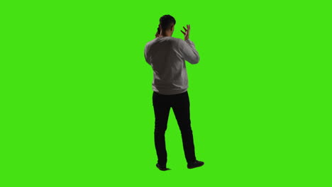 rear view of man talking on mobile phone standing against green screen with low key lighting