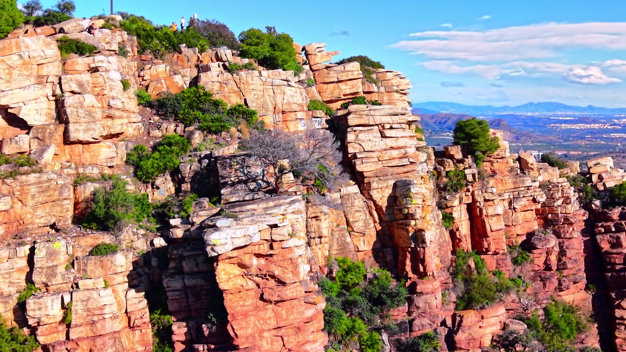 Detailed view of layered rock structures and textures with a distant city and sea on the horizon. Steep red sandstone cliffs with valley view. Aerial.
