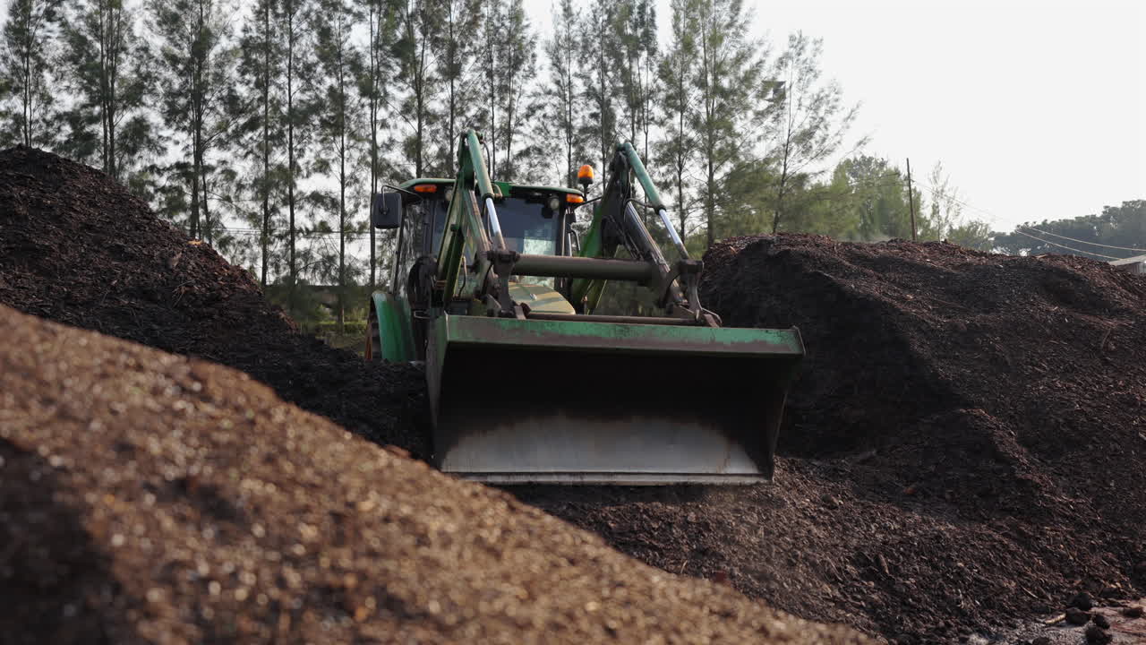 Trattore con caricatore frontale al lavoro in una fattoria, che carica sabbia e terra in una giornata di sole, agricoltura, operaio su macchina agricola, spazio per il testo.