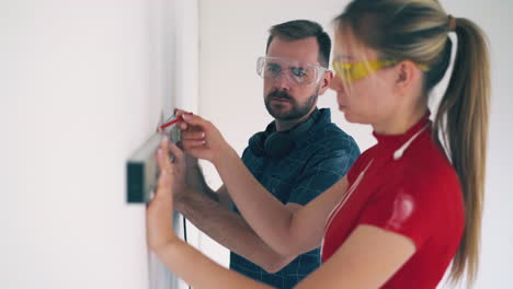 joyful couple checks wall using instrument in spacious room