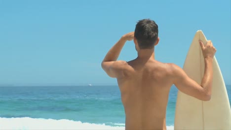 Man-holding-his-surfboard-and-looking-out-to-sea