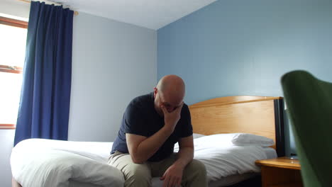 a desperate lonely man crying sitting on a bed with his head in his hand, appearing distressed or overwhelmed