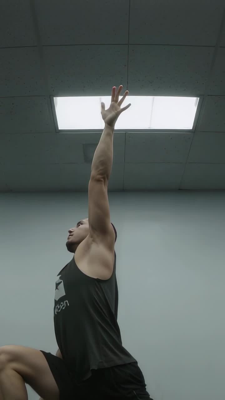 Uomo che sposta il peso in avanti e alza un braccio per uno stretching dell'anca sotto la luce del soffitto su un tappetino fitness