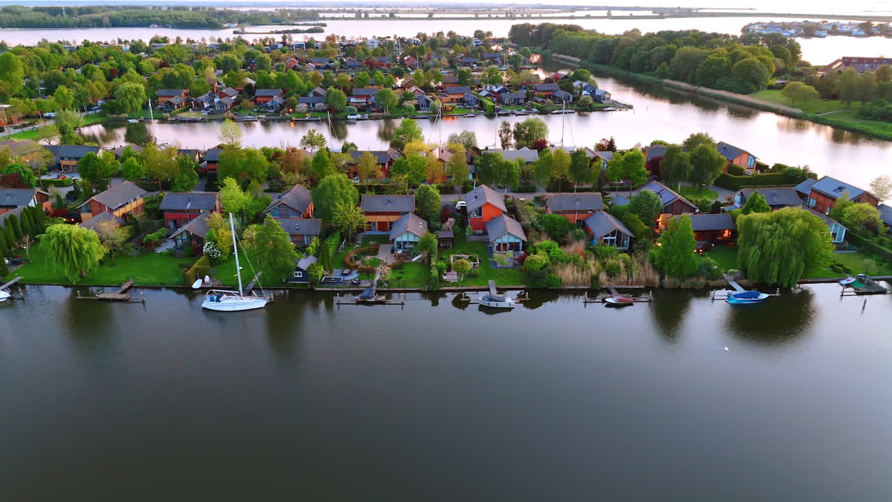 Flight over the canal along the green village. Boats and yachts near the waterfront. Countryside in the Netherlands.