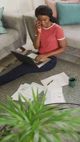 vertical video of african american woman sitting on floor and using laptop