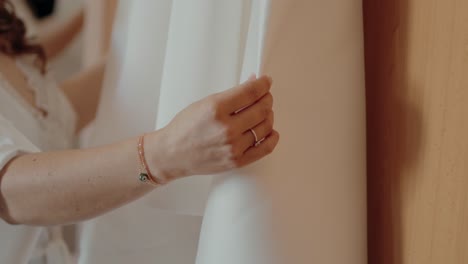 close up of hand with bracelet and ring gently holding white wedding dress fabric