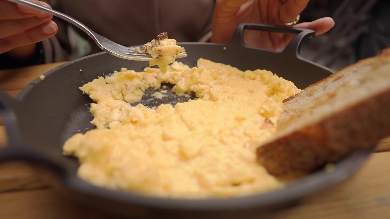 Person Eating Scrambled Eggs with Toast in a Cast Iron Skillet