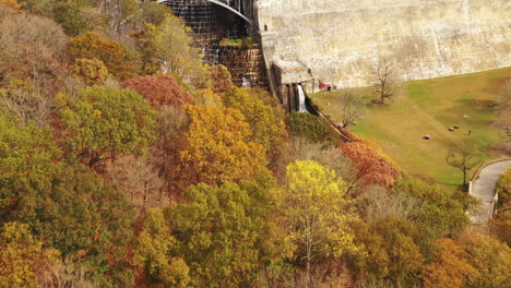 drone-dolly-in-shot-towards-the-waterfalls,-just-over-the-fall-colored-tree-tops-at-the-New-Croton-Dam-in-Westchester-County,-NY-on-a-cloudy-fall-morning