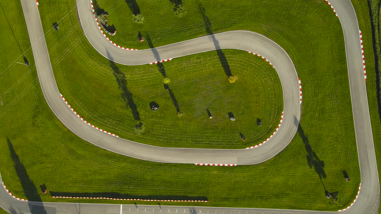 Top down aerial drone footage video flying higher and ascending over a go karting racing speedway track that is empty during sunset day while tree shadows are casting on the asphalt road