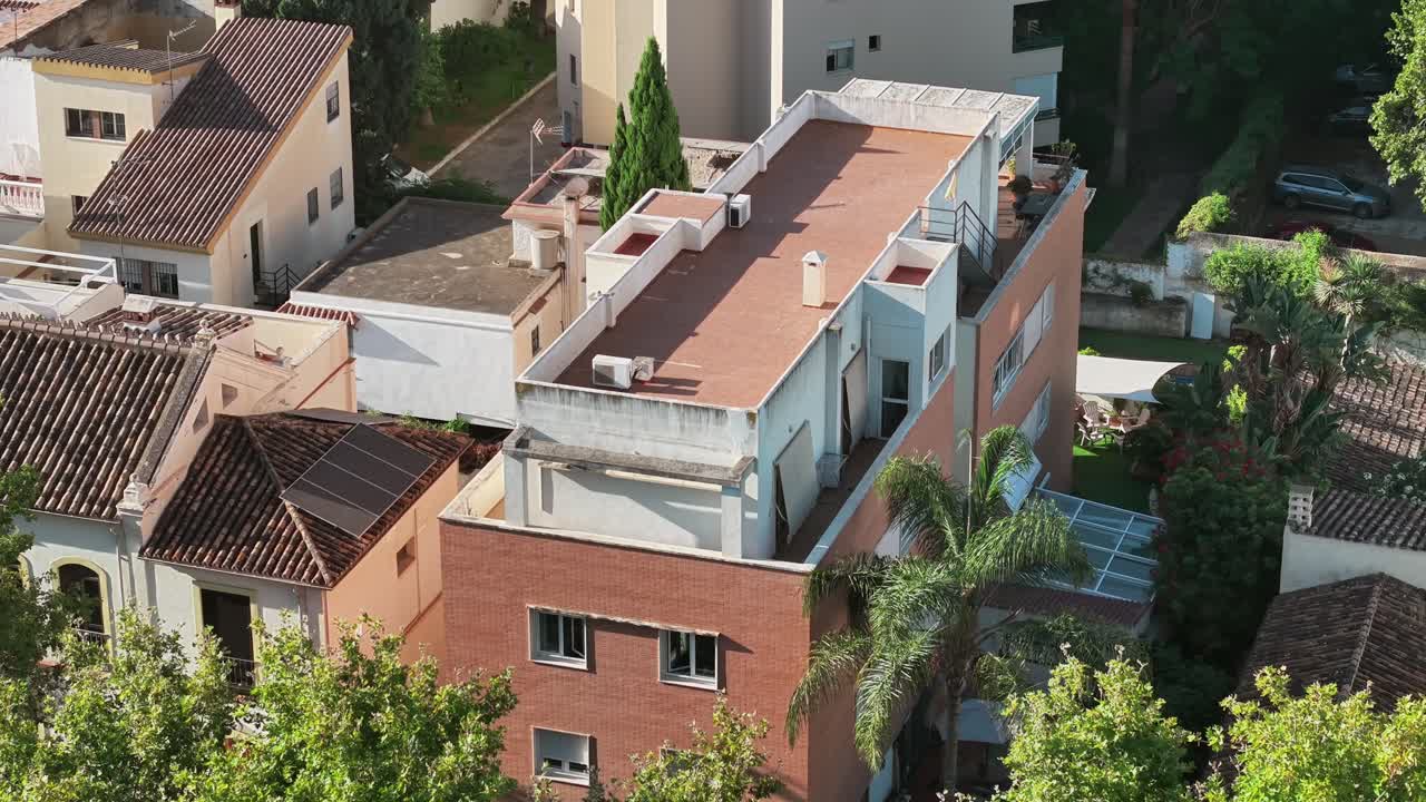 An aerial view of a Spanish residential area, showcasing a mix of brick and traditional tiled rooftops. Solar panels on the roof suggest a modern focus on sustainability and green energy