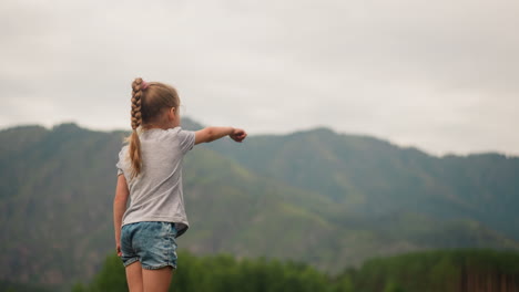 little child girl with braided hair points to mountains