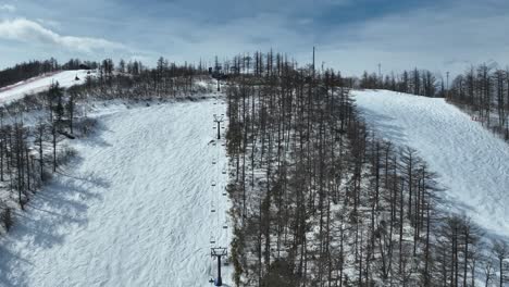 Ascending-drone-shot-flying-up-mountain-following-chair-lift-to-the-summit-of-the-snowy-covered-ski-mountain