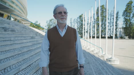 old man walking along building, looking aside, thinking